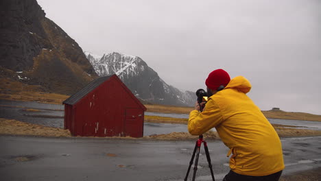 fotógrafo tomando fotos de cabaña roja con paisaje montañoso en noruega
