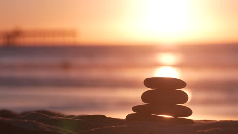 stack of pebble stones, sandy ocean beach, sunset sky. rock balancing by water.