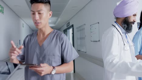 diverse doctors and nurses using tablets and walking through corridor at hospital, in slow motion