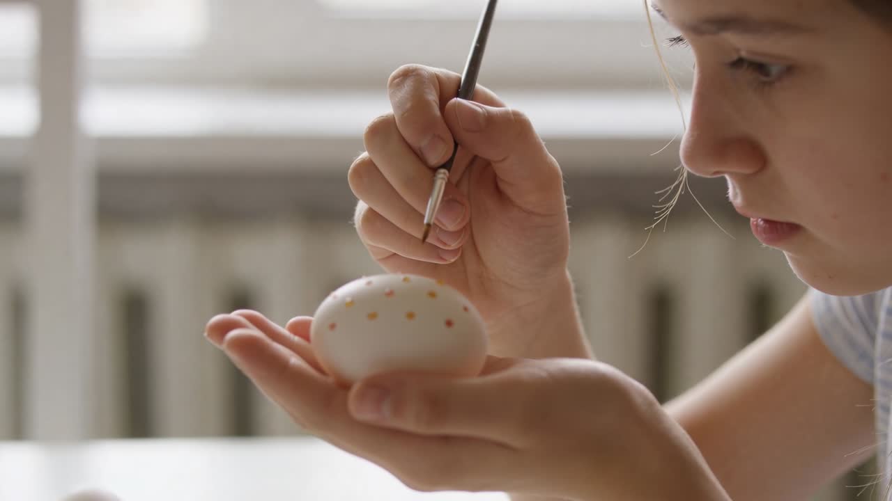 Bringing brush, teen crafting white egg with gold dots at window table, striped top, copy space