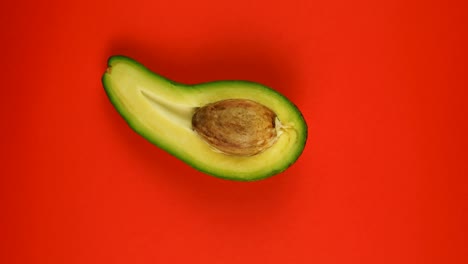 cortado en la mitad de aguacate o pera de cocodrilo girando rápidamente sobre fondo rojo.