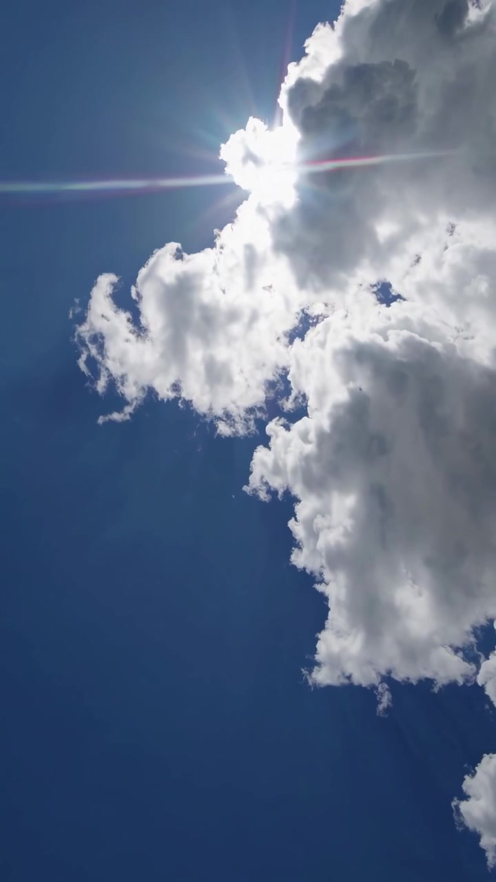 Bright Sun Shining Behind Moving White Clouds in Blue Sky