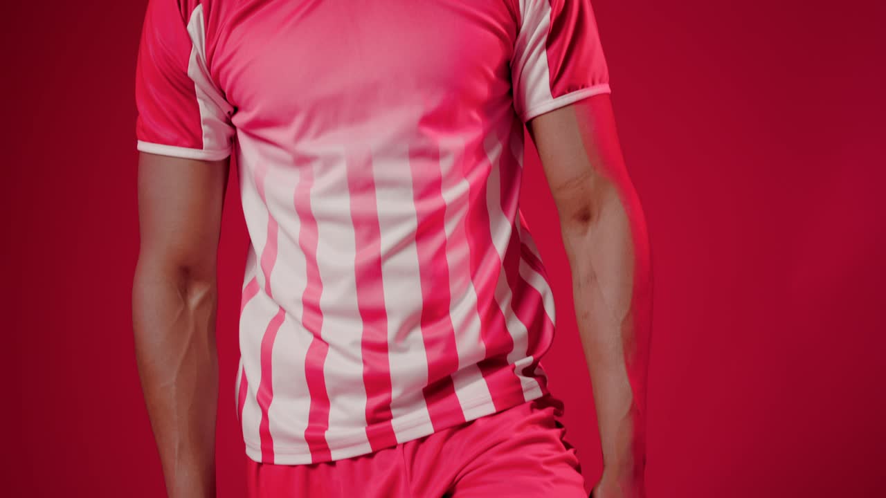 Câmera subindo revelando homem afro-americano equilibrando bola de futebol, posando para retrato em estúdio