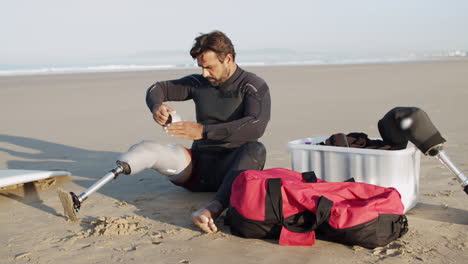 long shot of male surfer with disability taping artificial leg on the coast