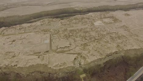 a drone shot moving backward of the ruins of jiaohe, xinjiang, by a grey day