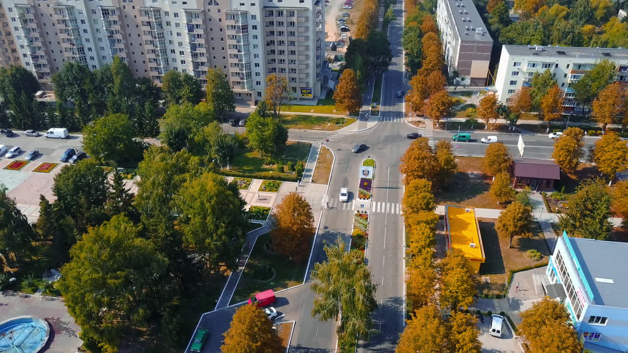 Cars and pedestrians moving by the city streets on sunny day. Residential area with green and orange trees in autumn.