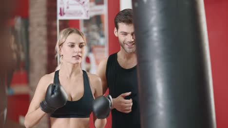 Sport-woman-boxing-punching-bag-in-gym-club-with-personal-trainer.