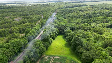 Crane-shot-of-a-steam-train-snaking-its-way-through-the-Great-British-countryside-on-its-way-to-dover-with-steam-coming-out-of-the-engine