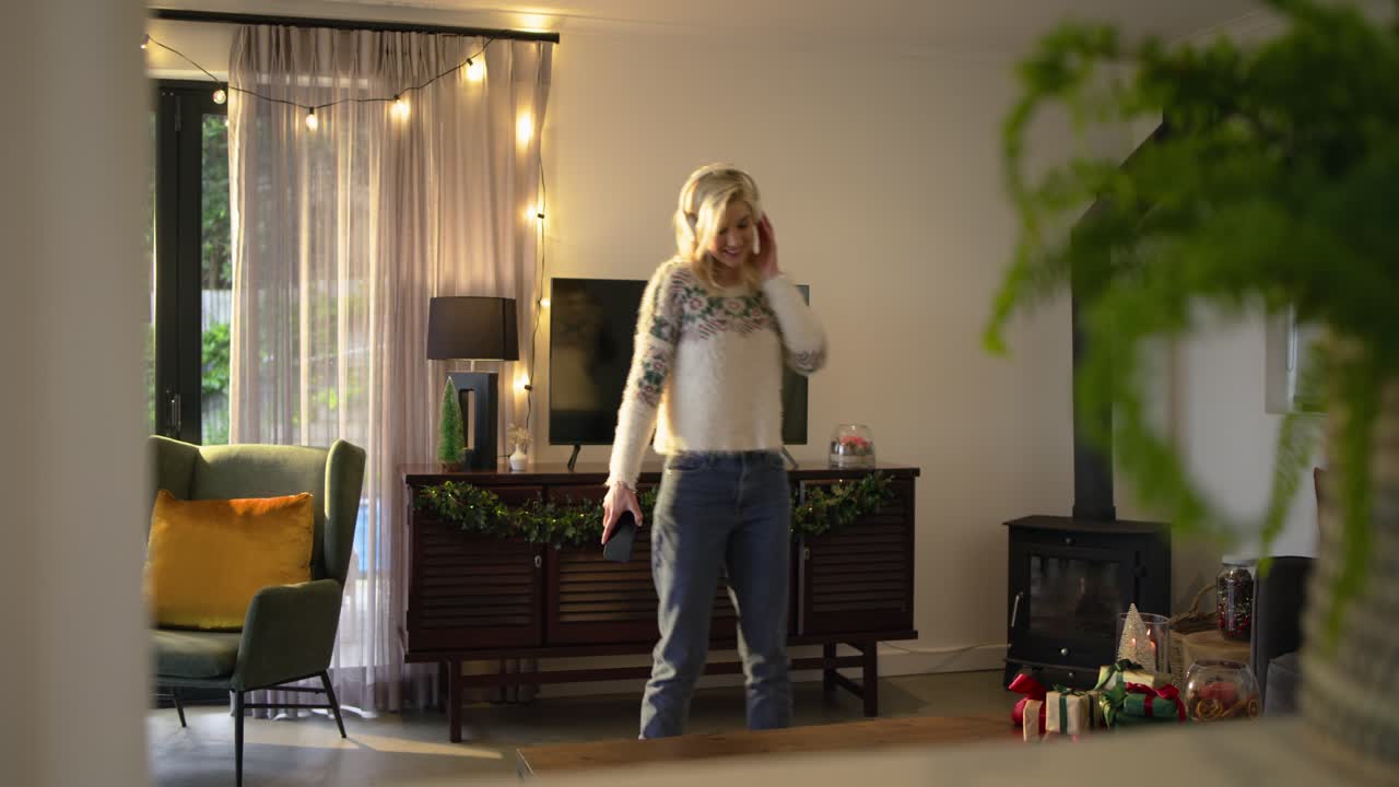 Music starting headphone-wearing woman dancing, pressing smartphone making call in living room