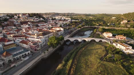 Roman-bridge-over-Arade-River,-Silves-city-surrounded-by-green-fields-and-trees,-Algarve