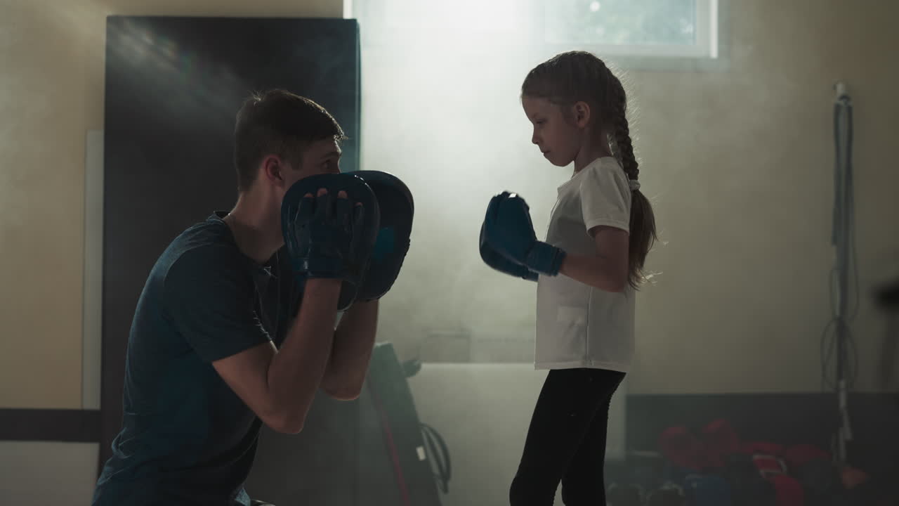 체육관에서 아이들에게 전투 기법을 가르치는 코치, 손바닥을 고 권투 강사, 무술 수업에서 스포츠 클럽에서 작은 소녀와 이야기하는 느린 동영상