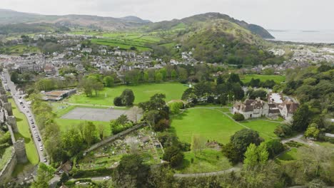 a large number of sailboats and motor vessels are moored at the long jetty in the fast flowing river off the english town of conwy among the green hills of wales on a cloudy day backwards drone dolley