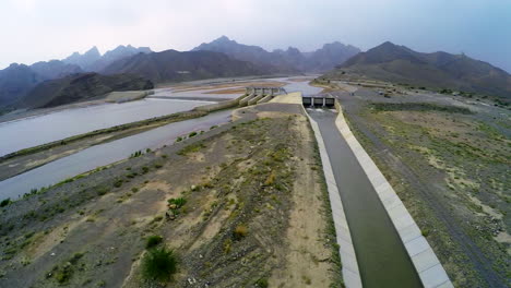 Aerial-view-of-spillway-of-a-dam,-Beautiful-majestic-mountains-in-the-back-of-the-dam