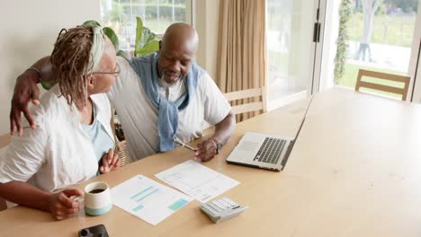 Happy-african-american-senior-couple-doing-paperwork-using-laptop-at-home,-slow-motion