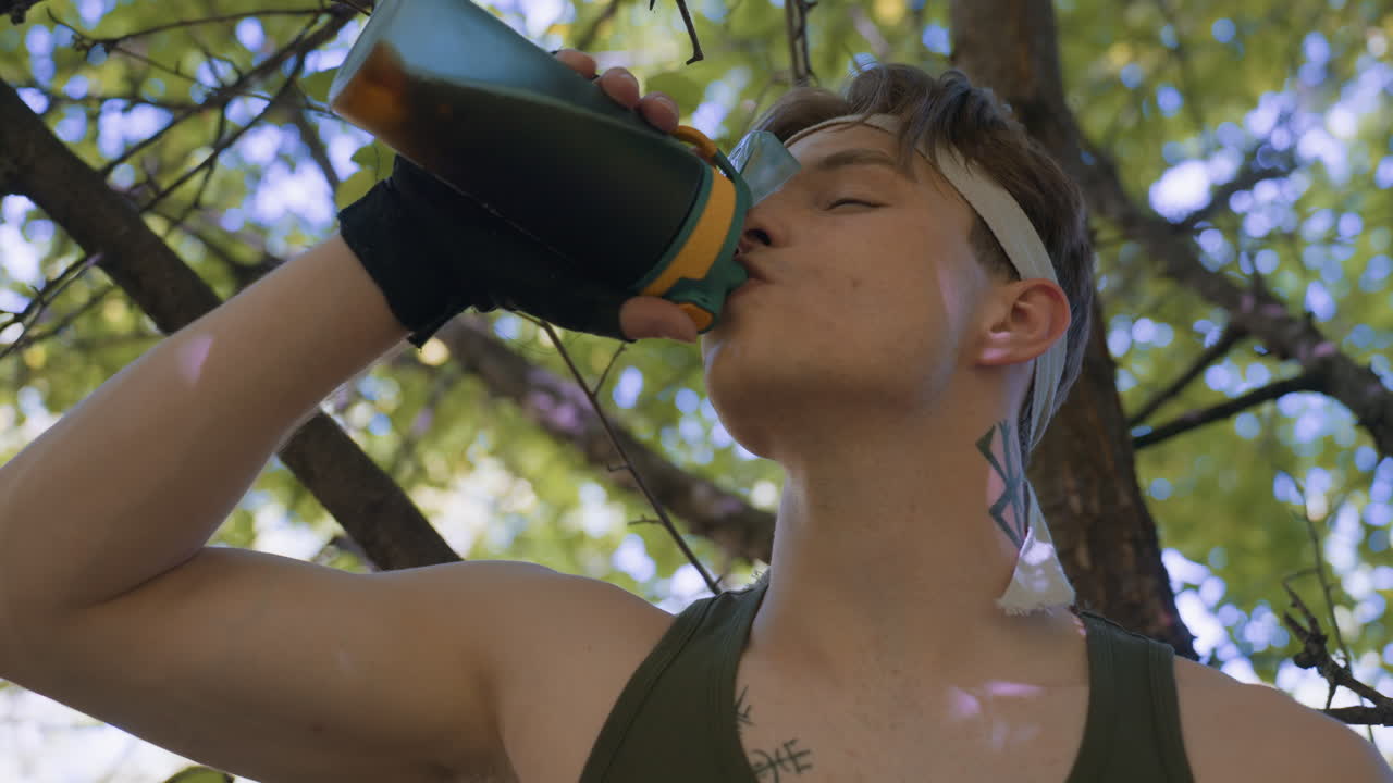 warrior exhales gently while sipping coffee under leafy canopy, eyes closed and throat moving in relief, wearing headband holding bottle, dappled sunlight filtering through green leaves