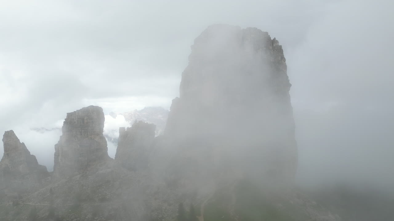 Misty fog swirling around rugged Cinque Torri peaks, revealing dramatic Dolomites landscape under shifting atmospheric veils in Italian alpine wilderness