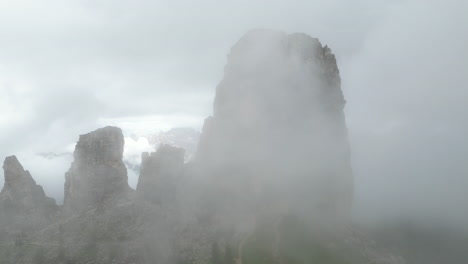 misty fog swirling around rugged cinque torri peaks, revealing dramatic dolomites landscape under shifting atmospheric veils in italian alpine wilderness