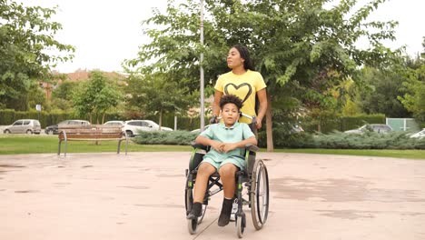 woman pushing a boy in a wheelchair through a park
