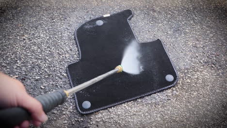 man washing a dirty car mat with a hose