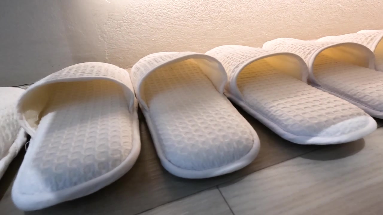 Een rij witte slippers met wafeltextuur staat op een houten vloer onder warme verlichting.