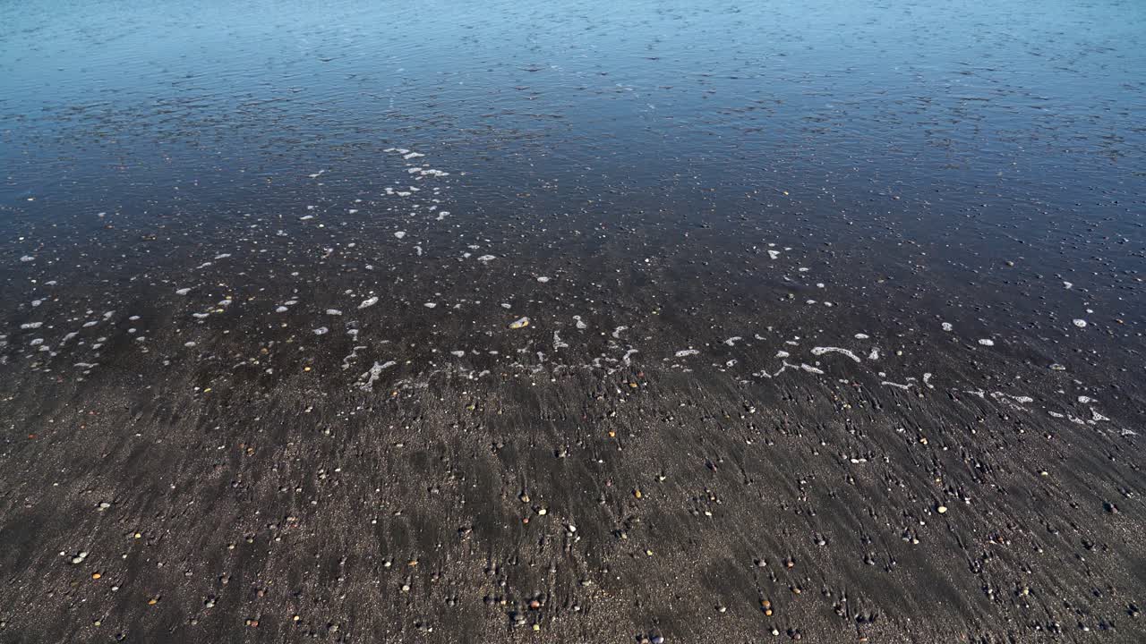 Calm water flowing off a black sand beach in Iceland on a cold and sunny day in the land of fire and ice