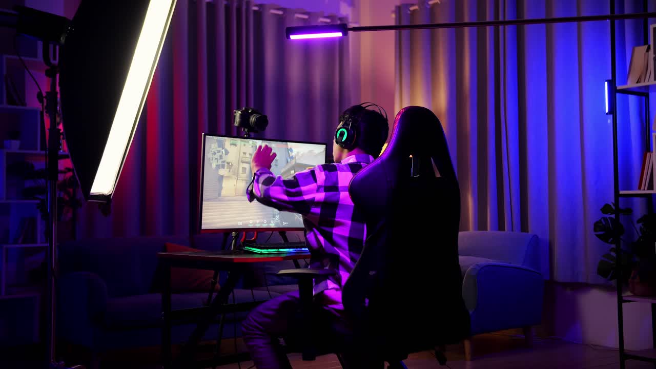 Back View Of Asian Boy Streamer Stretching While Playing Game Over Network On Personal Computer. Live Stream Video Game, Desk Illuminated By Rgb Led Strip Light