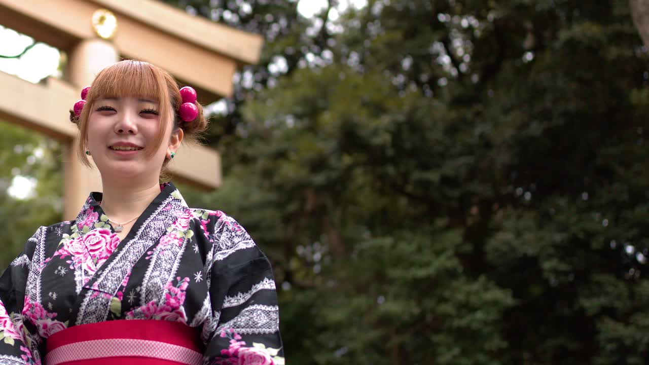 Una Donna Giapponese in Yukata Floreale Sorride e Parla Davanti a un Cancello Torii di Legno