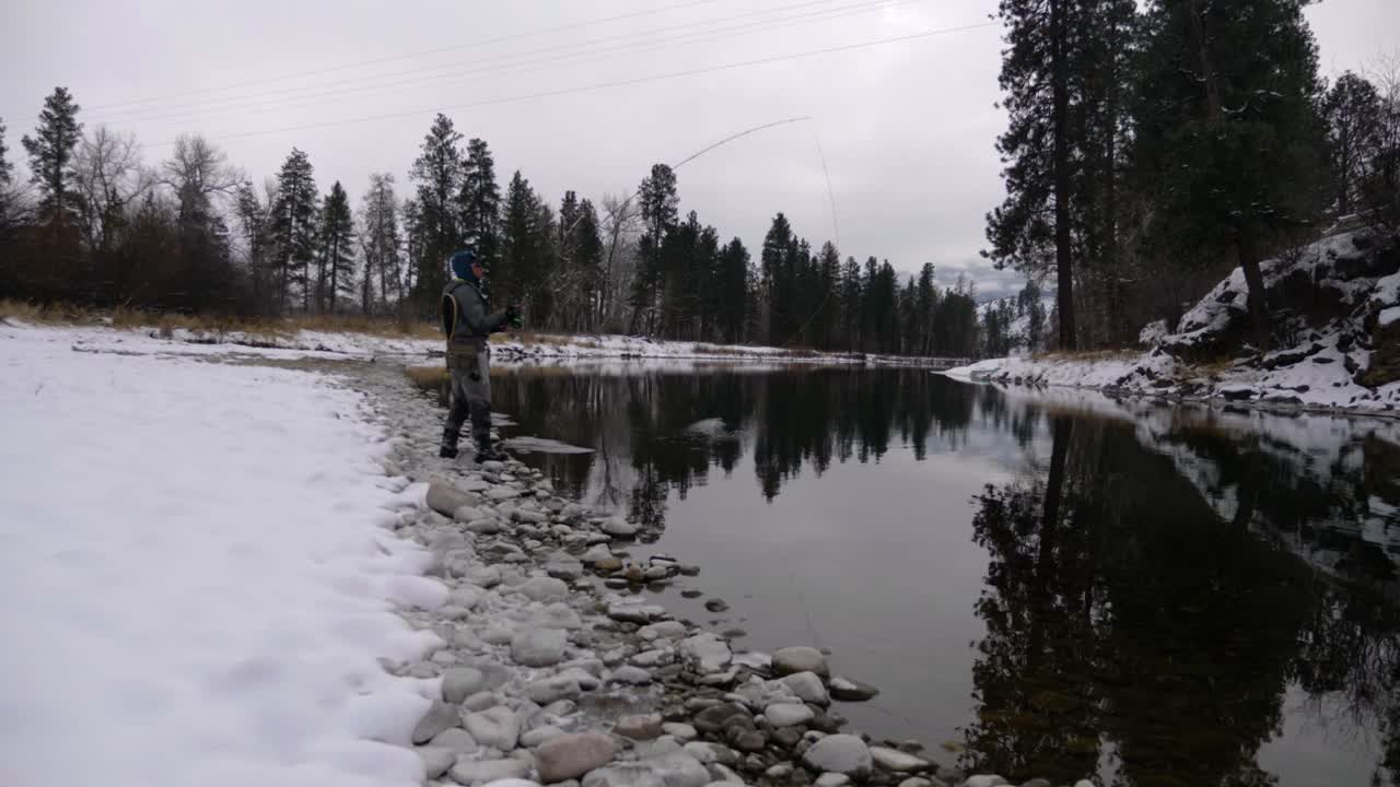 hombre asiático pescando con mosca en pleno invierno en el río con orillas cubiertas de nieve