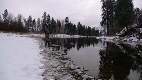 asian man fly fishing in the dead of winter on the river with snow-covered banks