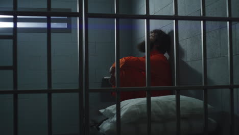 prisionero en uniforme naranja se sienta en la cama en la prisión