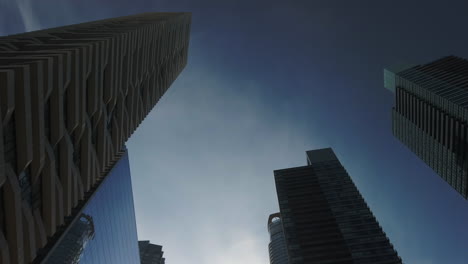 wide travelling shot looking straight up at modern vertical buildings set against the sky