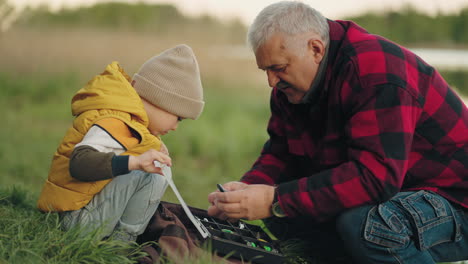 curious-little-boy-is-viewing-fishing-gear-of-his-grandfather-granddad-and-grandson-on-fishing