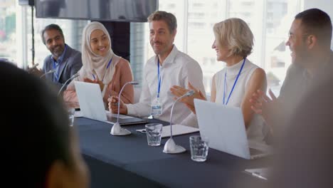 a panel of business delegates applauding colleague at a conference