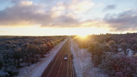 aerial of beautiful sunrise remote frozen highway as car passes underneath, 4k