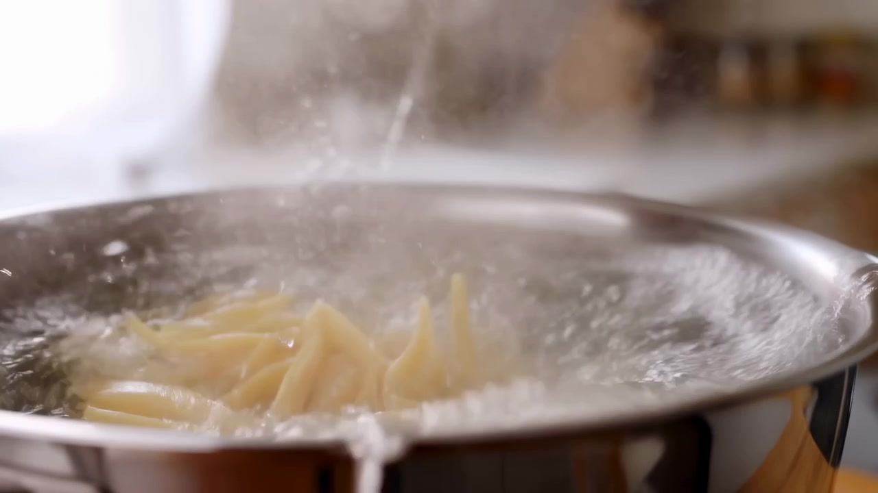 Spaghetti freschi lasciati cadere in acqua bollente, pentola d'acciaio inossidabile che bolle con vapore, primo piano di fili che affondano.