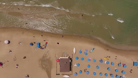 Summer-day-at-the-beach-with-people-in-the-water-and-under-colorful-umbrellas,-Top-down-drone-footage