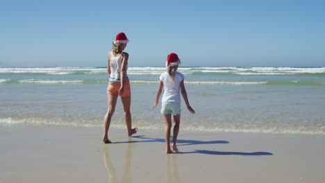 mother and daughter walking on shore at beach on a sunny day