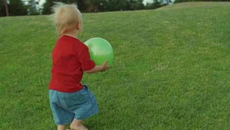 adorable toddler going on green field barefoot. boy holding ball in hands