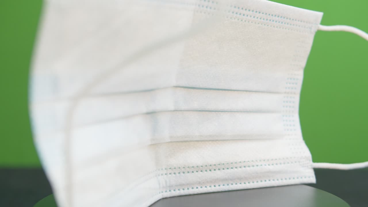 primer plano de una mascarilla quirúrgica desechable que gira frente a una pantalla verde