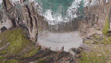 Top-down-drone-pull-out-of-waves-lapping-against-the-rocky-North-Atlantic-coastline-of-England,-highlighting-the-interplay-between-land-and-sea