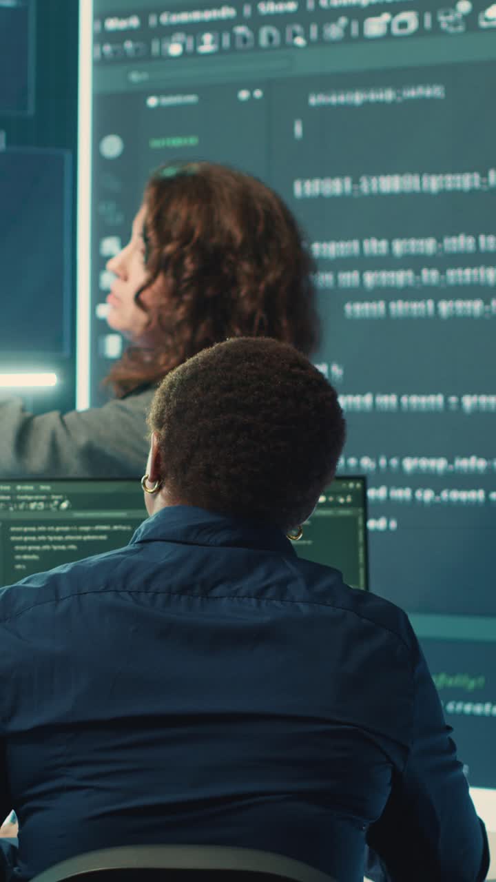 Programmers Discussing Code on Multiple Screens in Dark Office