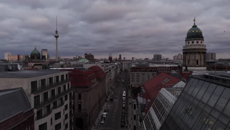 Fly-above-street-in-town.-Cityscape-with-famous-landmarks-towering-above-roofs.-Franzosischer-and-Berliner-Dom-and-Fernserturn-against-overcast-sky.-Berlin,-Germany