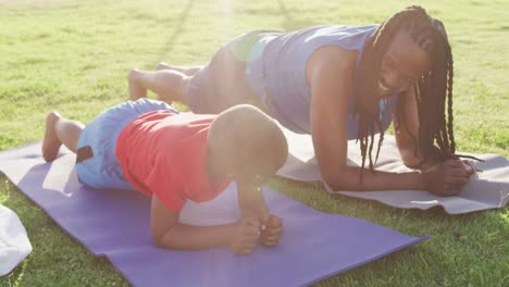 video of happy african american son and father doing plank on grass on sunny day