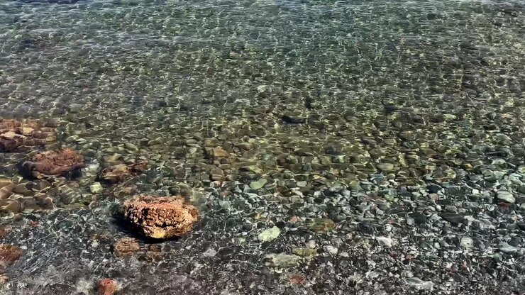 Transparent shallow water over a rocky beach on Crete Island, Greece, with sunlight reflections