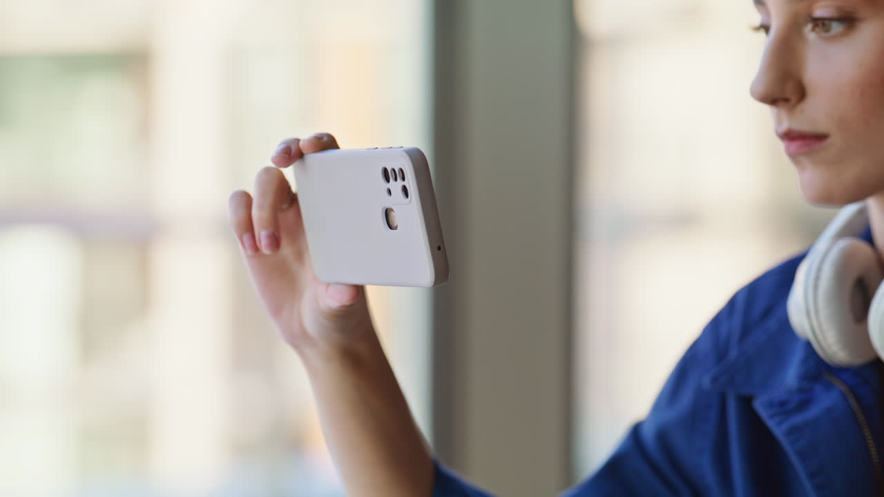 Girl browsing smartphone video sitting by cafeteria panoramic window closeup