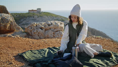 Girl-enjoying-cliff-picnic-alone-vertical.-Curly-tourist-admire-ocean-landscape