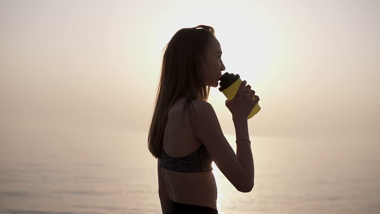 ⁇ 은 파란 하늘과  ⁇ 빛을 배경으로 물을 마시고 조 ⁇ 하는 긴 머리 여성 달리기 선수