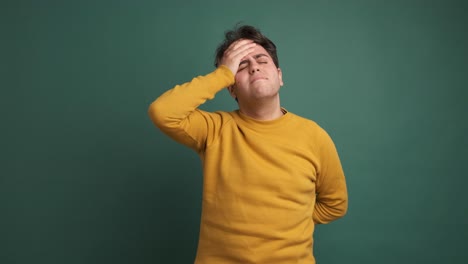 frustrated man suffering from headache in green studio