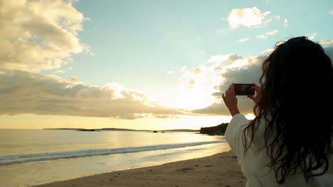 brunette taking a photo of the sunset on her smartphone