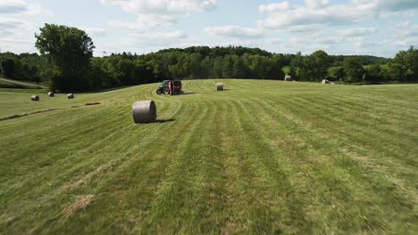 tractor harvesting field with straw harvester many round hay bale, aerial